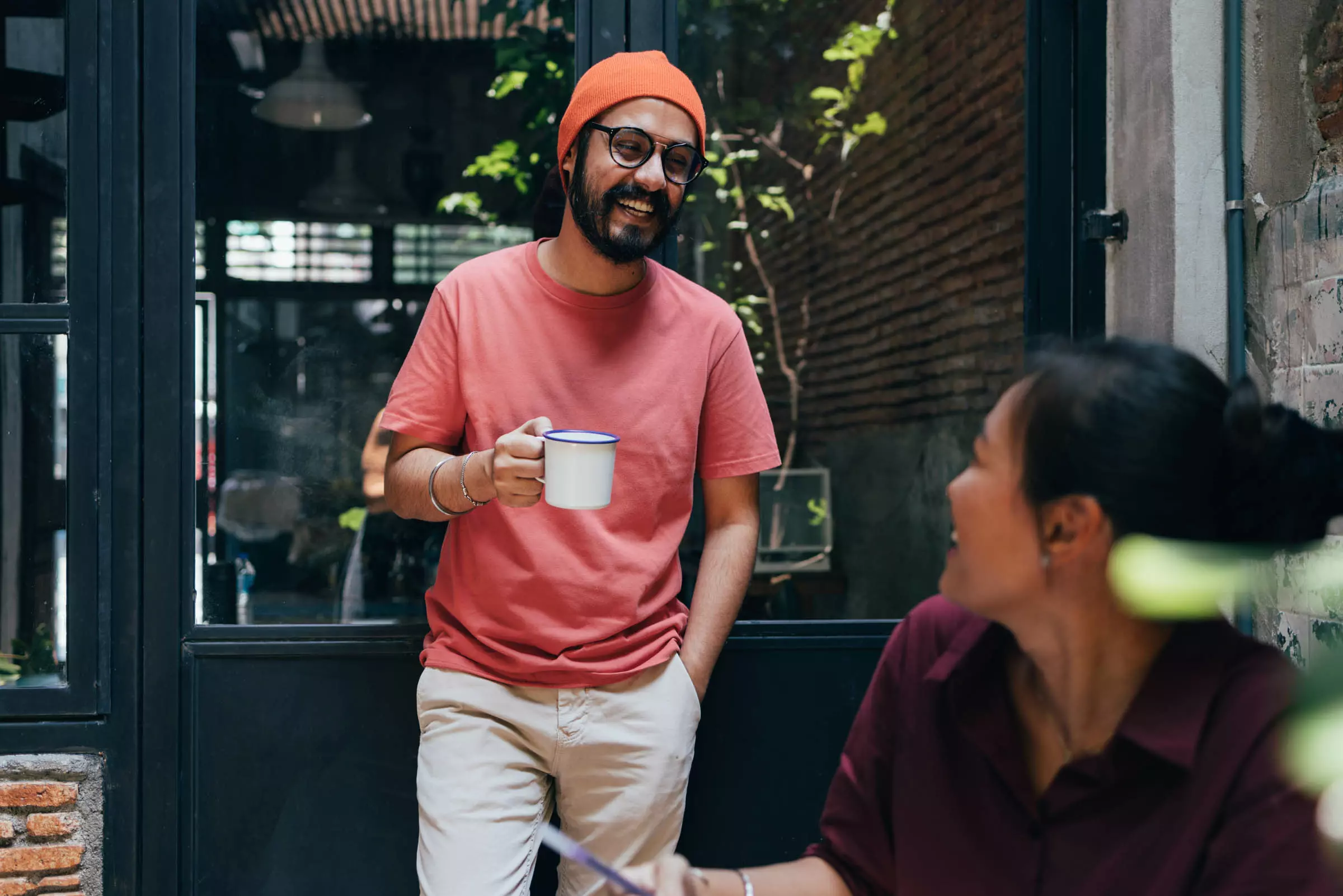 Man holding a coffee mug while talking with a woman on a patio